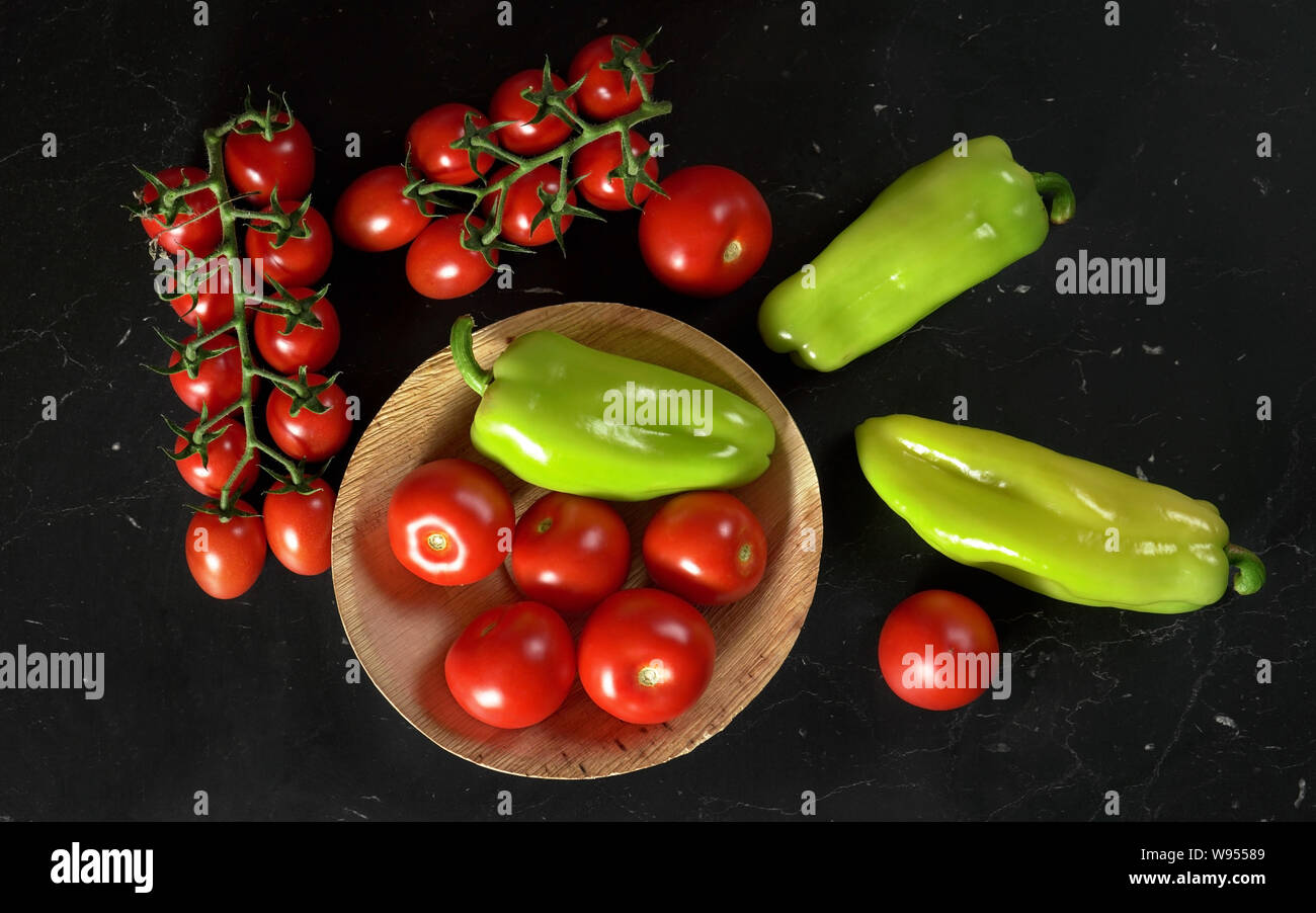 Tomatoes and green bell peppers in small bowl and on black board, view from above Stock Photo