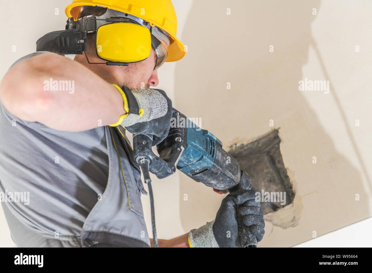 Caucasian Worker Chiseling Concrete. Wearing Hard Hat and Noise Protection Headphones. Stock Photo