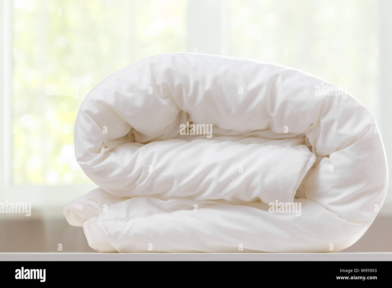A folded white duvet lies on a table on a blurred background. Stock Photo