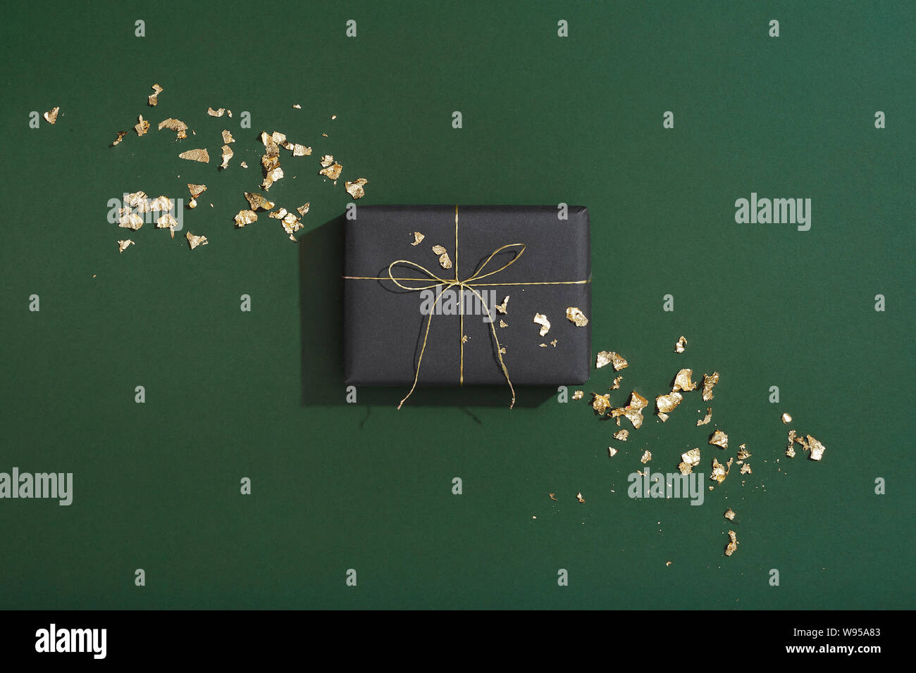 Black Christmas gift and gold flakes on green background, masculine present flat lay Stock Photo