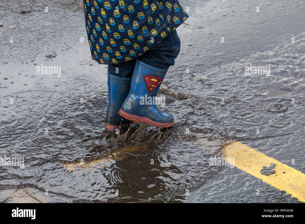 Kid in rain boots jumping in a puddle Stock Photo