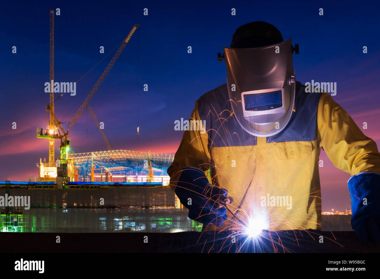 Industrial worker welding steel structure for infrastructure building project with construction site in background. Stock Photo