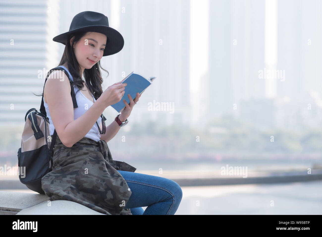 Beautiful asian tourist woman reading the travel guide book searching for for tourists sightseeing spot. Vacation travel in summer. Stock Photo