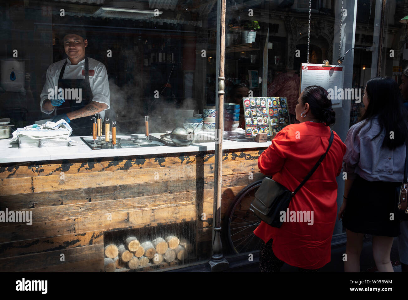 Chinese Restaurant Chef Works In The Open Kitchen As Tourists Look At The Menu Outside In Chinatown In Soho London United Kingdom The Present Chinatown Is In The Soho Area Occupying The Chinese Restaurant Chef Works In The Open Kitchen As Tourists Look At The Menu Outside In Chinatown In Soho London United Kingdom The Present Chinatown Is In The Soho Area Occupying The