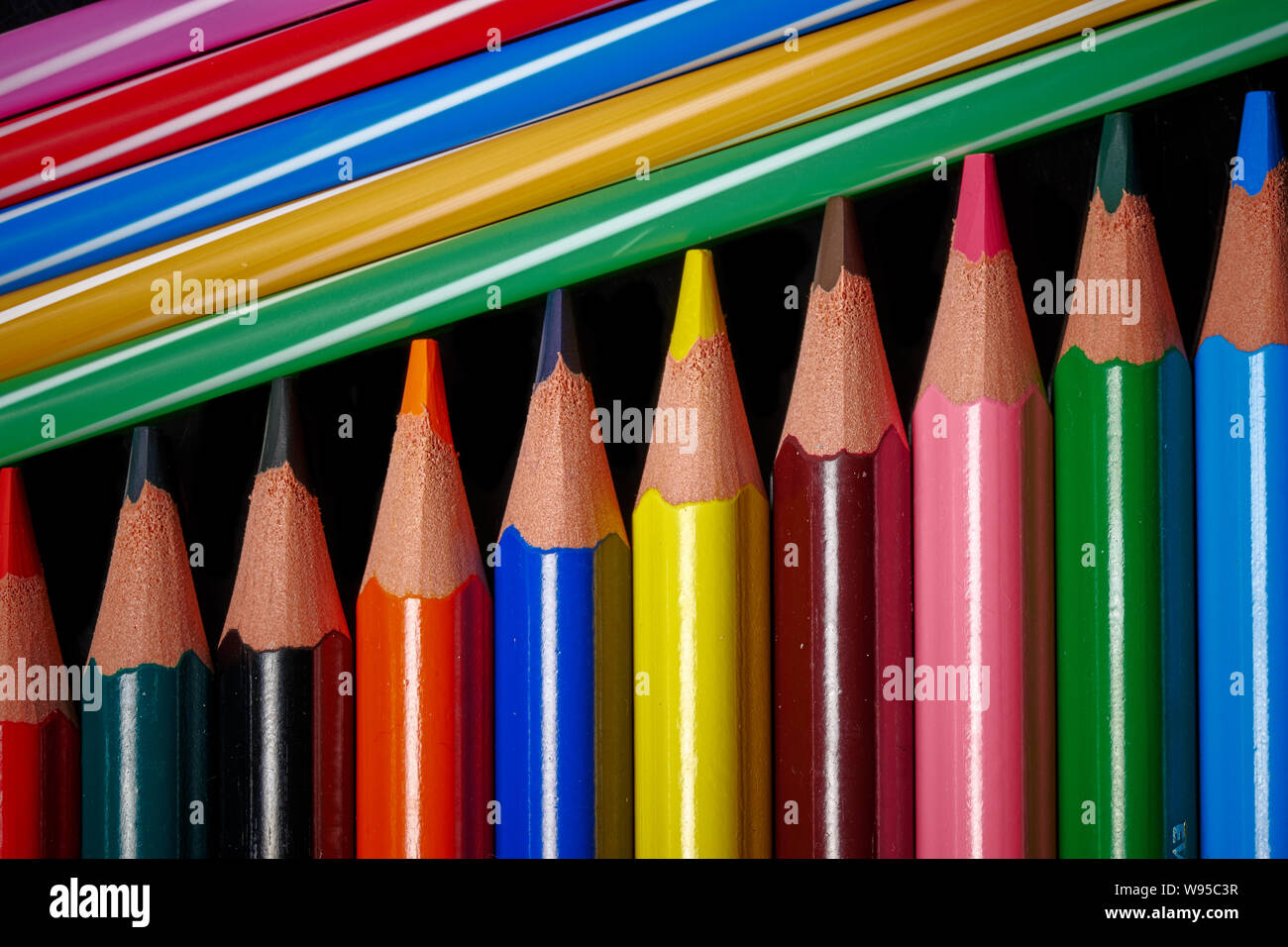 Colored pencils in a row with drinking straws isolated on black background Stock Photo