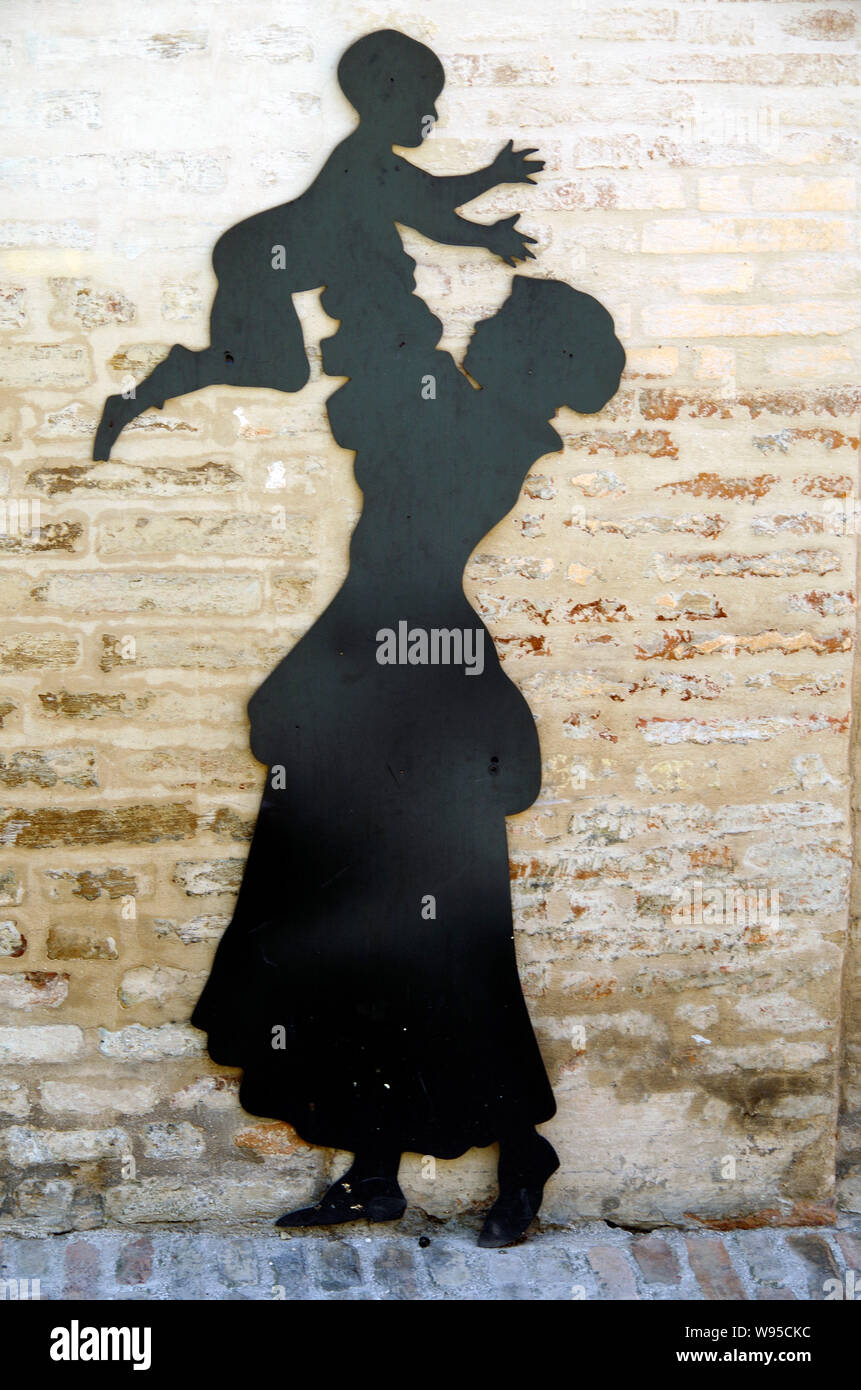 Life-sized silhouette, steel plate painted black, fixed to a brick wall, showing an apparently joyful mother holding her small child above her head, Stock Photo