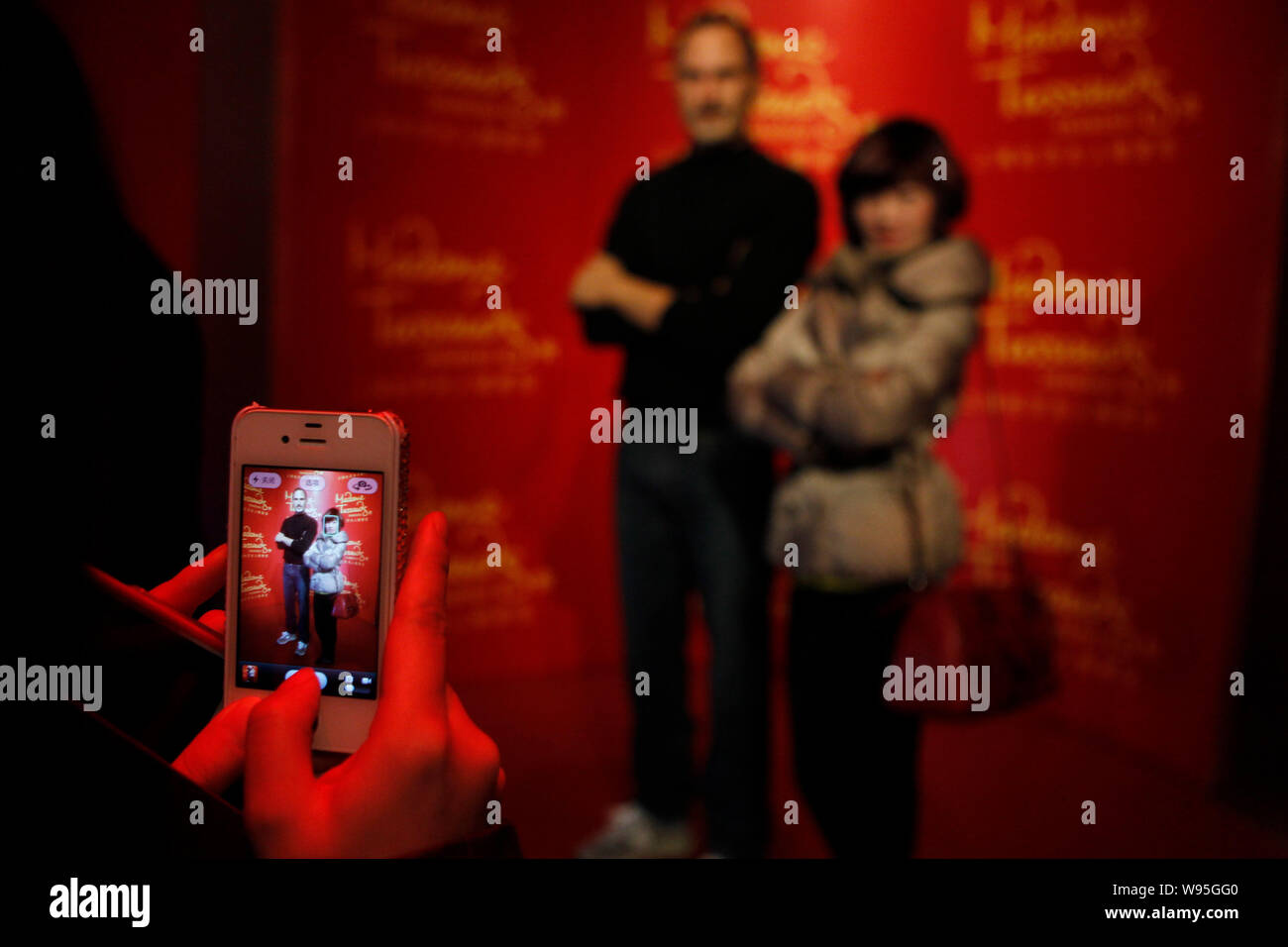A visitor uses an iPhone 4S smartphone to take photos of another posing with the wax figure of Steve Jobs at Madame Tussauds in Shanghai, China, 24 De Stock Photo