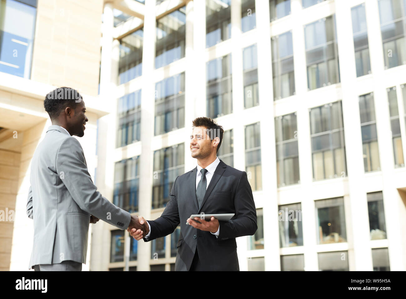 Two confident business partners in suits standing and shaking hands to each other in the city outdoors Stock Photo
