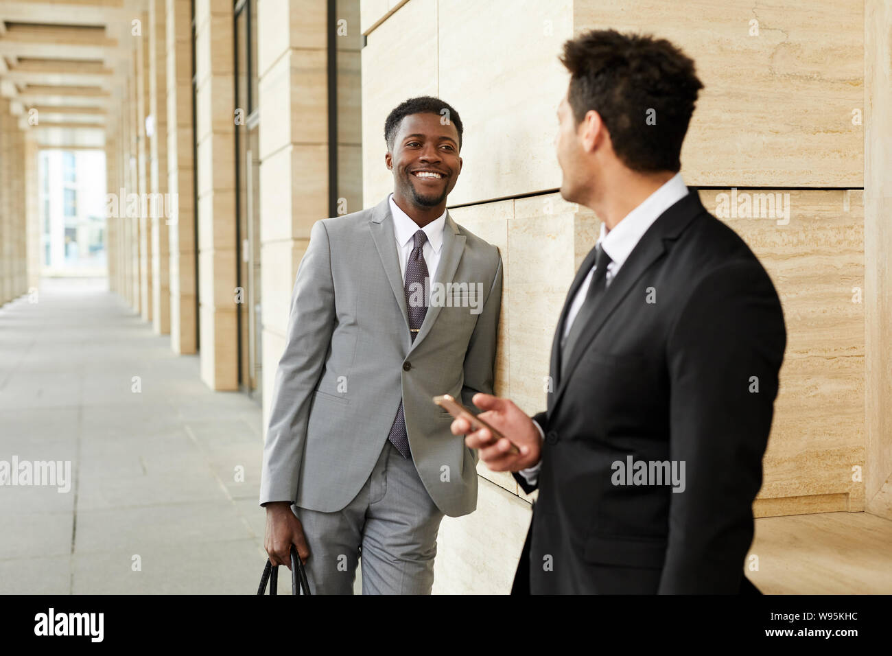 Young African businessman in suit smiling to his colleague while they standing outdoors in the city Stock Photo