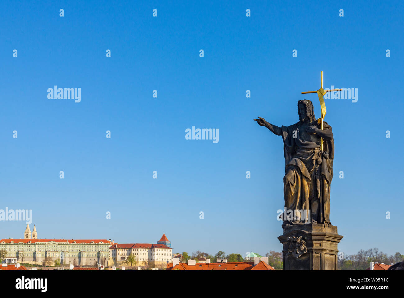 view of Statue of Saint  John the Baptist stand on pedestal and balustrades of Charles Bridge over Vltava river and background of Praha Castle. Stock Photo