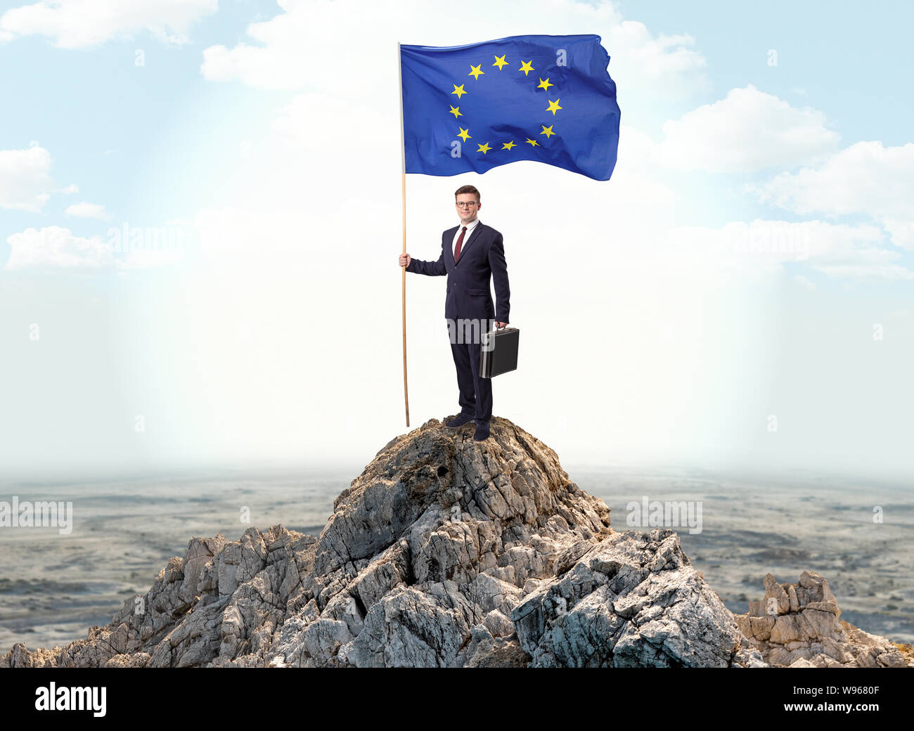 Successful businessman on the top of a mountain holding victory flag ...