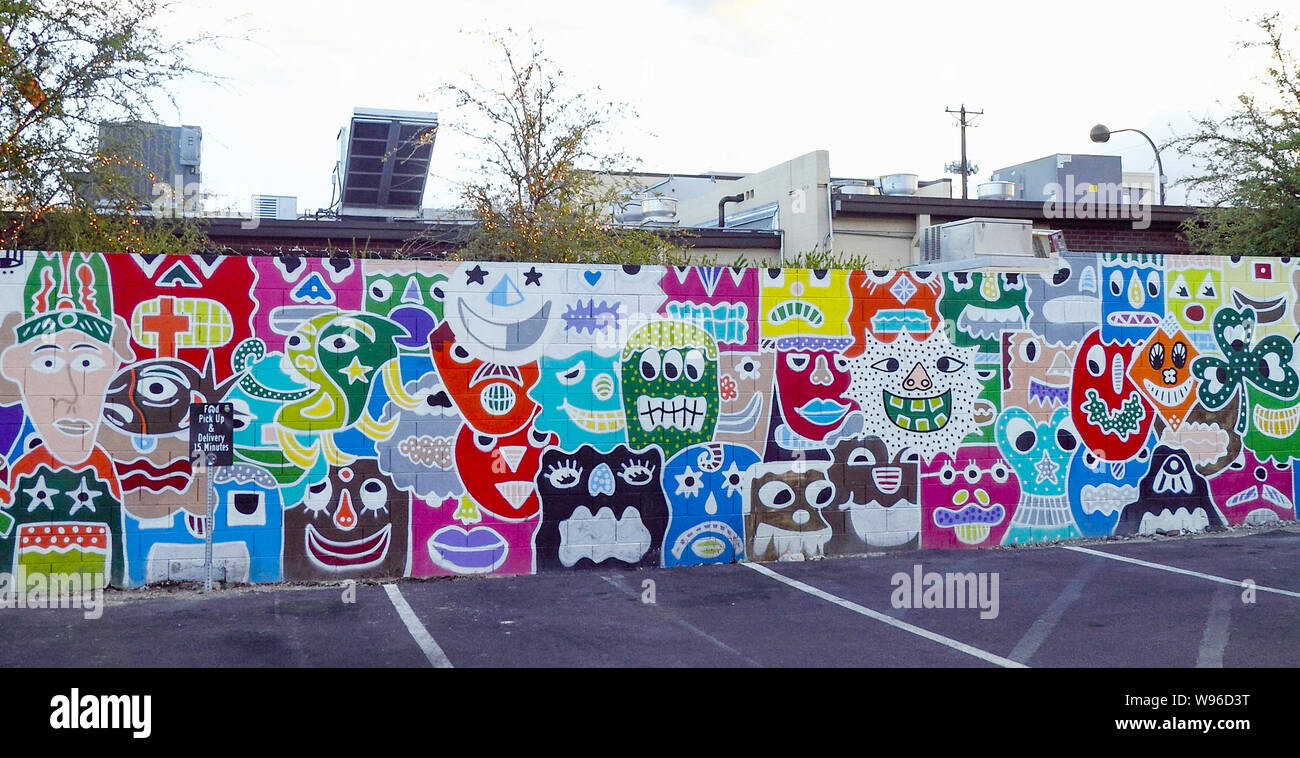 Concreate wall decorated with faces and graffiti serving as a paring lot Stock Photo