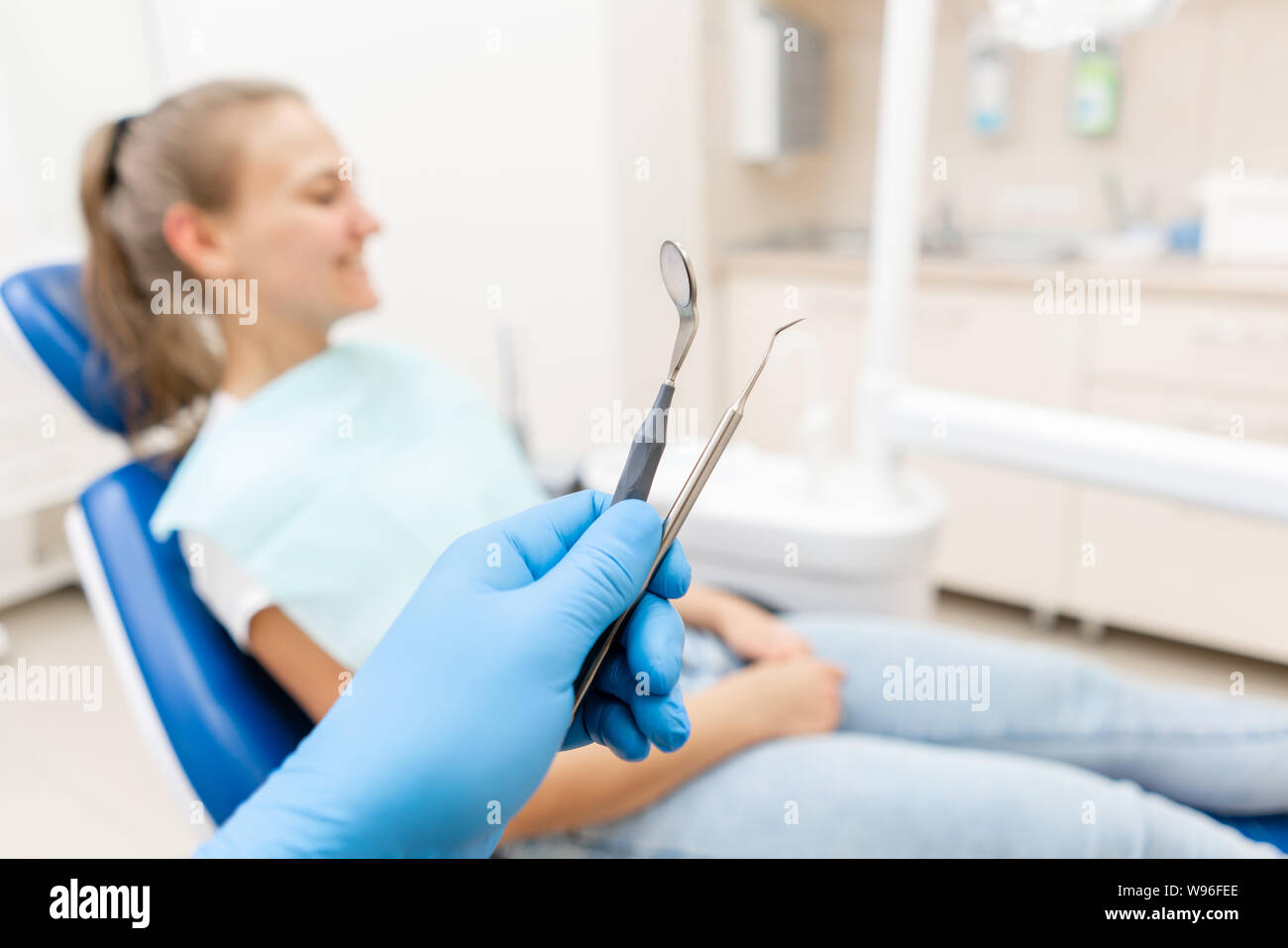 Close-up hand of dentist in the glove holds tool probe and mirror. The patient in the dental chair at the background. Dental work in clinic. Office Stock Photo