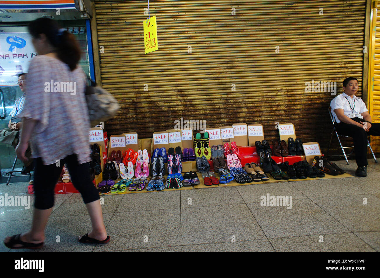 A Woman Walks Past A Vendor Selling Shoes And Slippers In