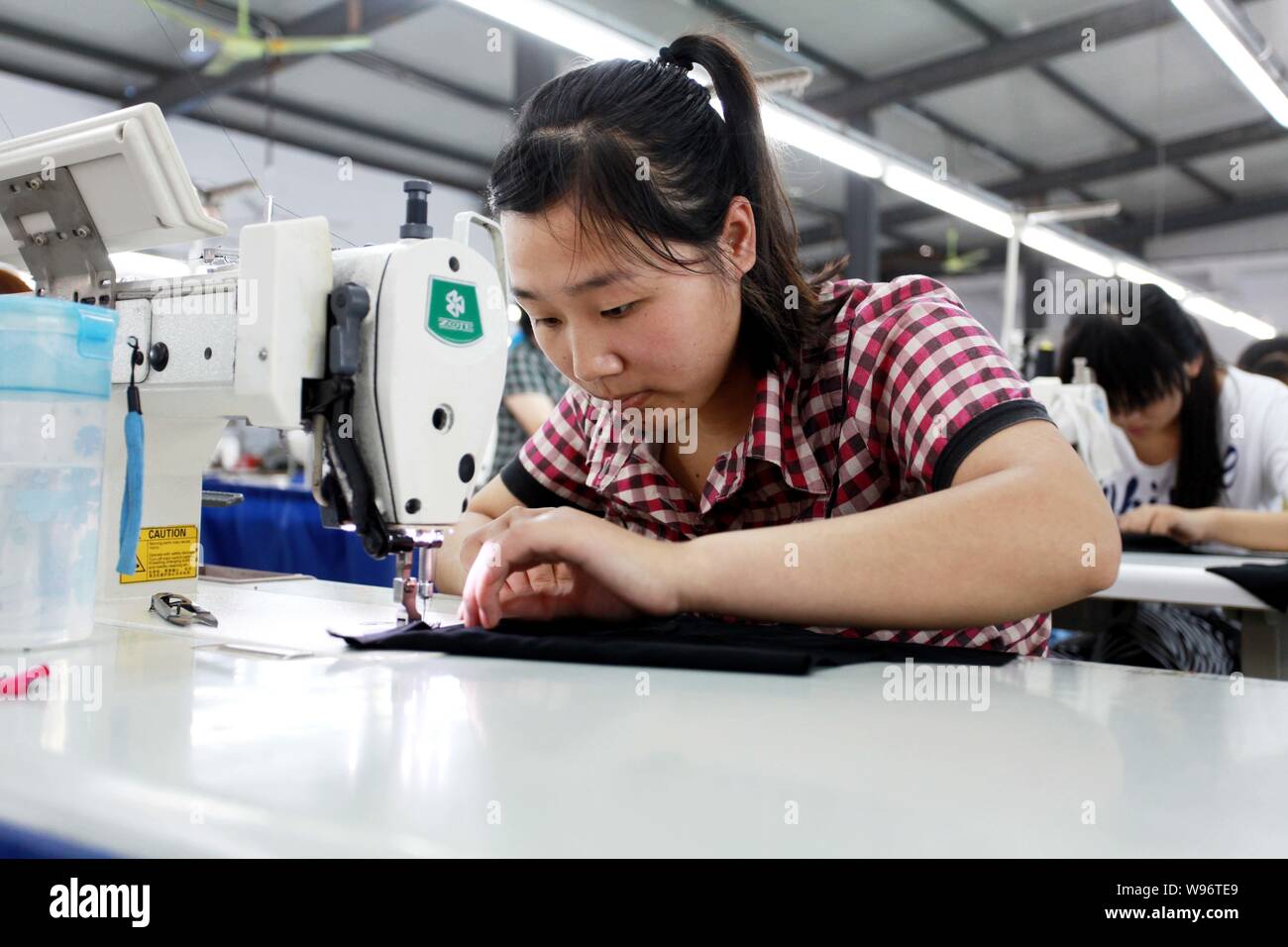 A female Chinese worker handles the production of cloth on a sewing machine in Huaibei city, east Chinas Anhui province, 6 July 2012.   Chinese textil Stock Photo