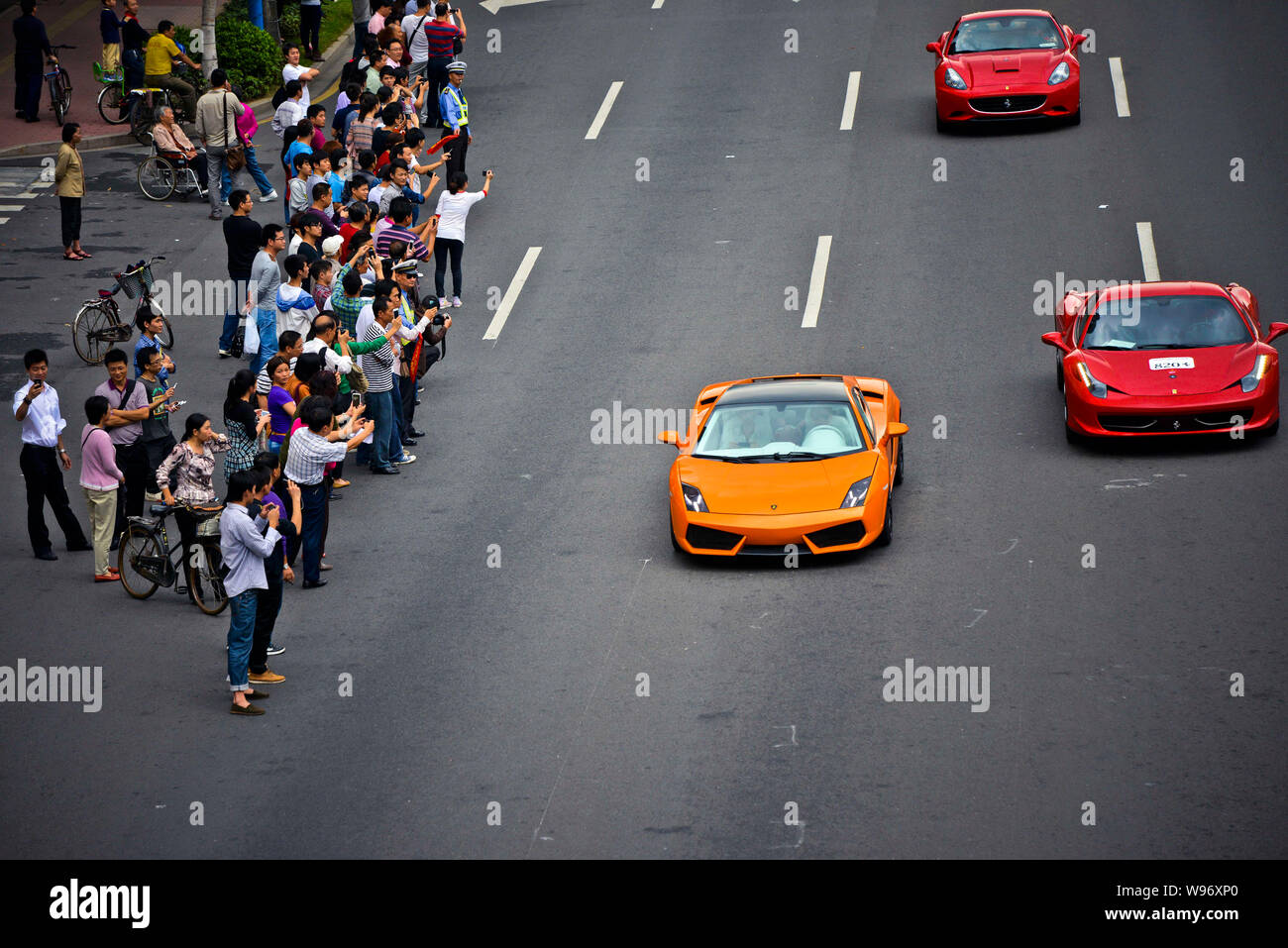 Onlookers take photos of Ferrari sports cars travelling on the road during a parade to celebrate the 20th anniversary of Ferraris presence in China, i Stock Photo