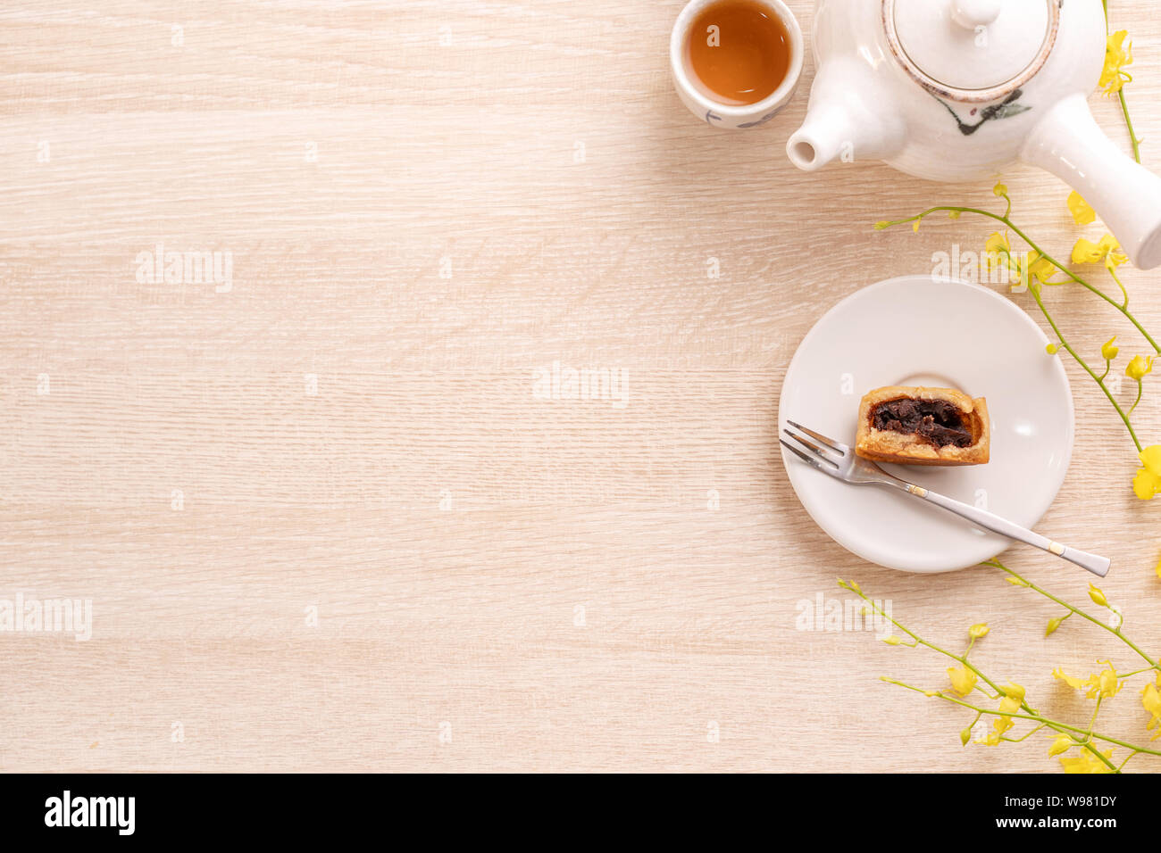 Tasty moon cake for Mid-Autumn festival on bright wooden table, concept of festive afternoon tea decorated with yellow flowers, top view, flat lay. Stock Photo
