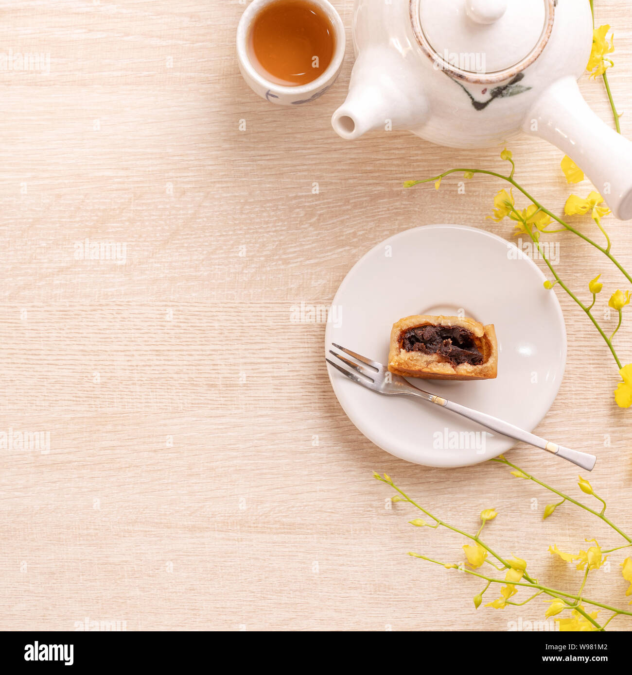 Tasty moon cake for Mid-Autumn festival on bright wooden table, concept of festive afternoon tea decorated with yellow flowers, top view, flat lay. Stock Photo