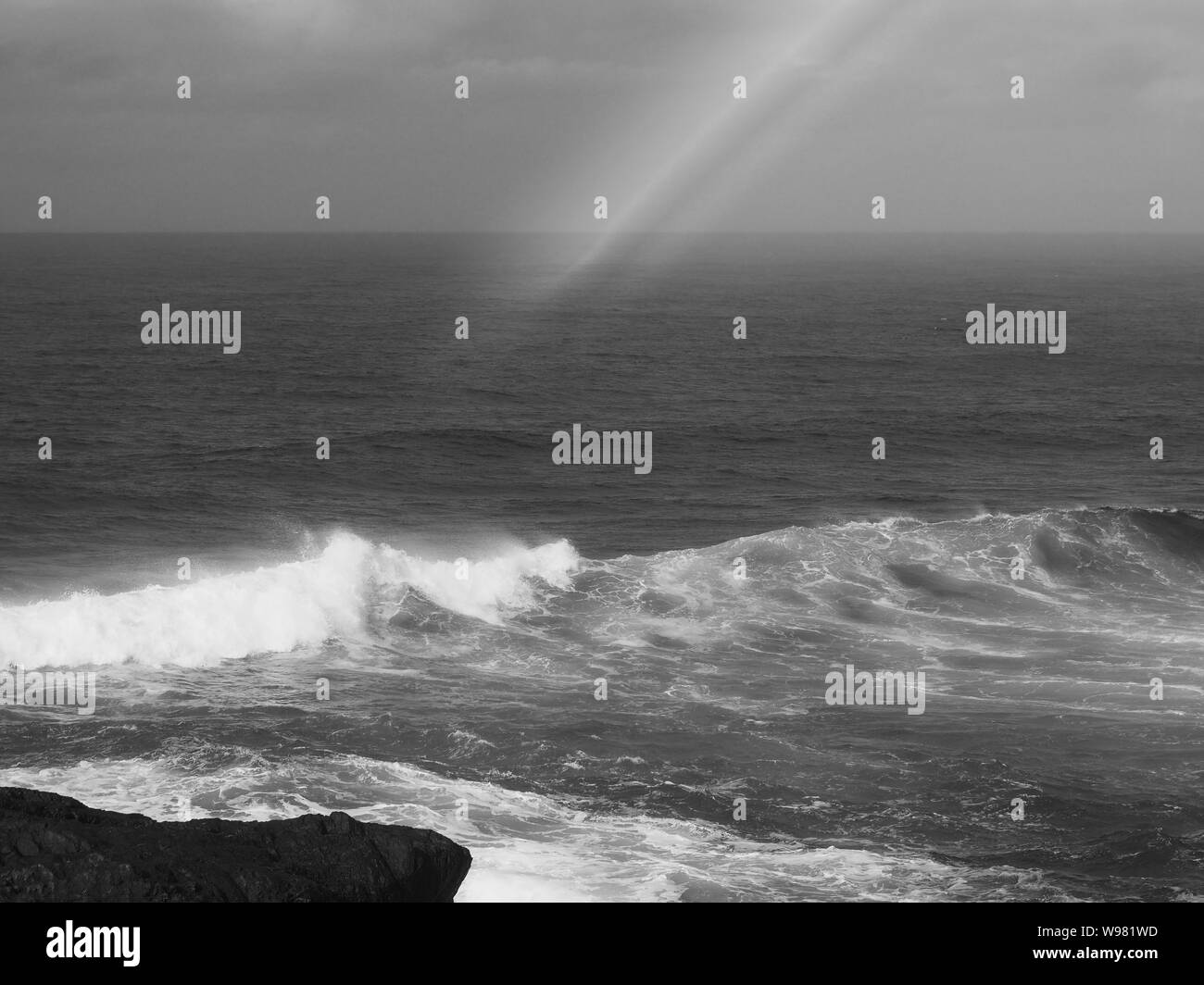 Surreal and dramatic. Black and white Rainbow over the ocean, waves breaking, with horizon in background Stock Photo