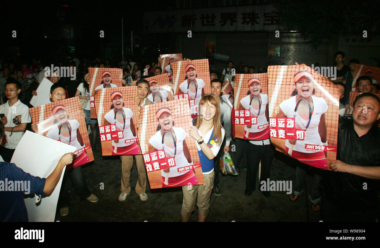 Local residents hold up posters of Chinese tennis star Li Na while watching the live broadcast of her competing against Francesca Schiavone of Italy d Stock Photo