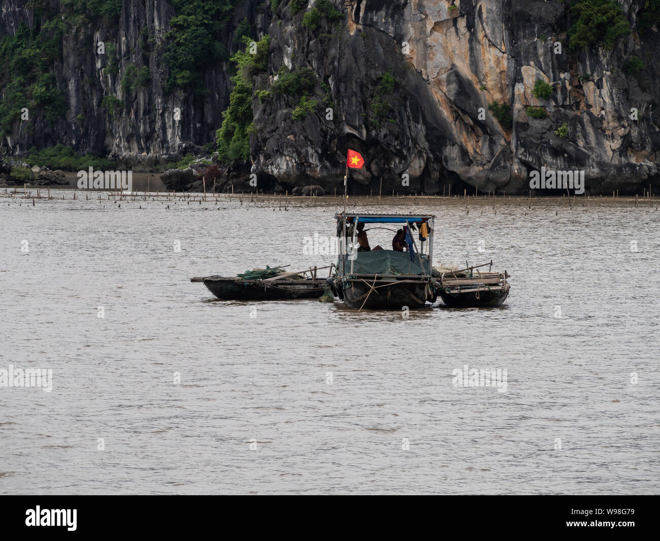 Traditional Vietnamese fishing boats out on the water in Ha Long Bay, northern Vietnam, flying Vietnamese flag Stock Photo
