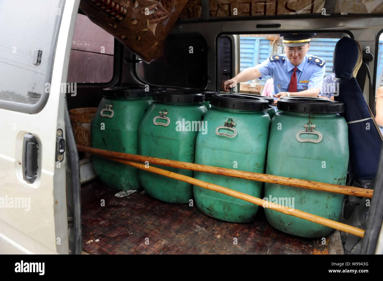 --FILE--A Chinese law enforcement officer puts barrels of waste oil in a van at an illegal workshop where cooking oil is made from waste oil dredged f Stock Photo