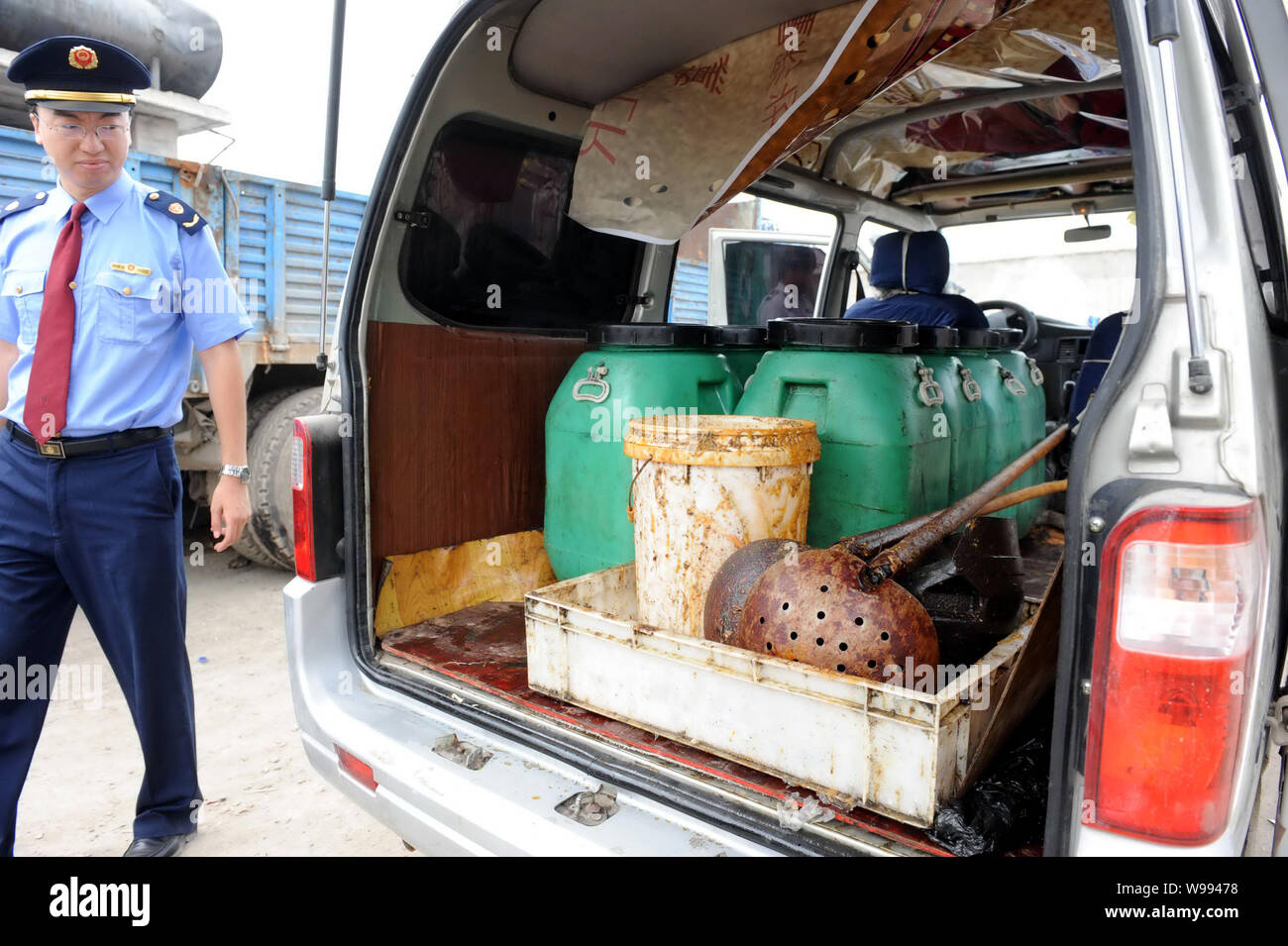 --FILE--A Chinese law enforcement officer walks past a van loaded with barrels of waste oil at an illegal workshop where cooking oil is made from wast Stock Photo