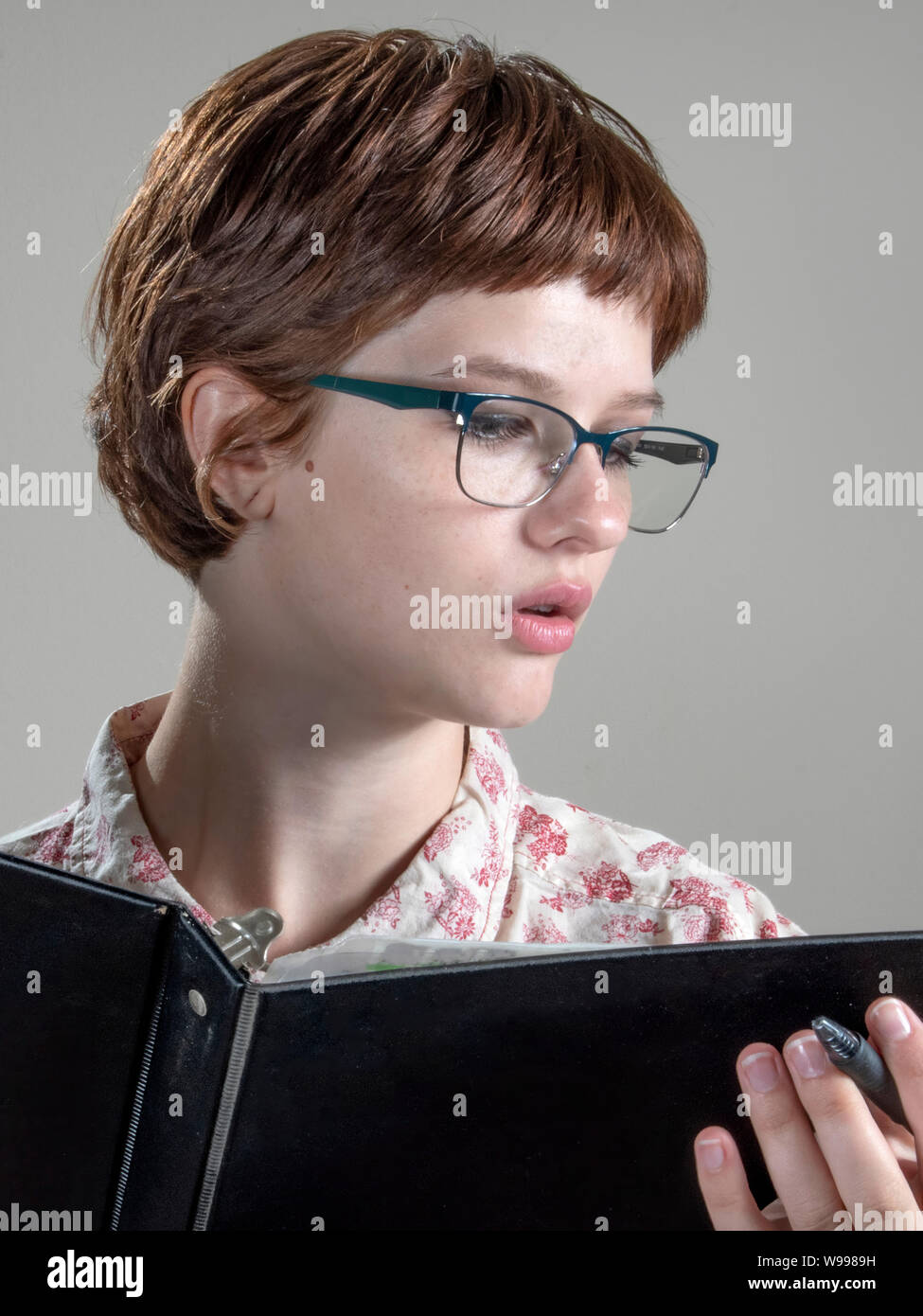 BOSSIER CITY, LA., U.S.A.. - AUG. 8, 2019: A pretty, young woman, pen in hand, peruses the content of a ring binder. Stock Photo
