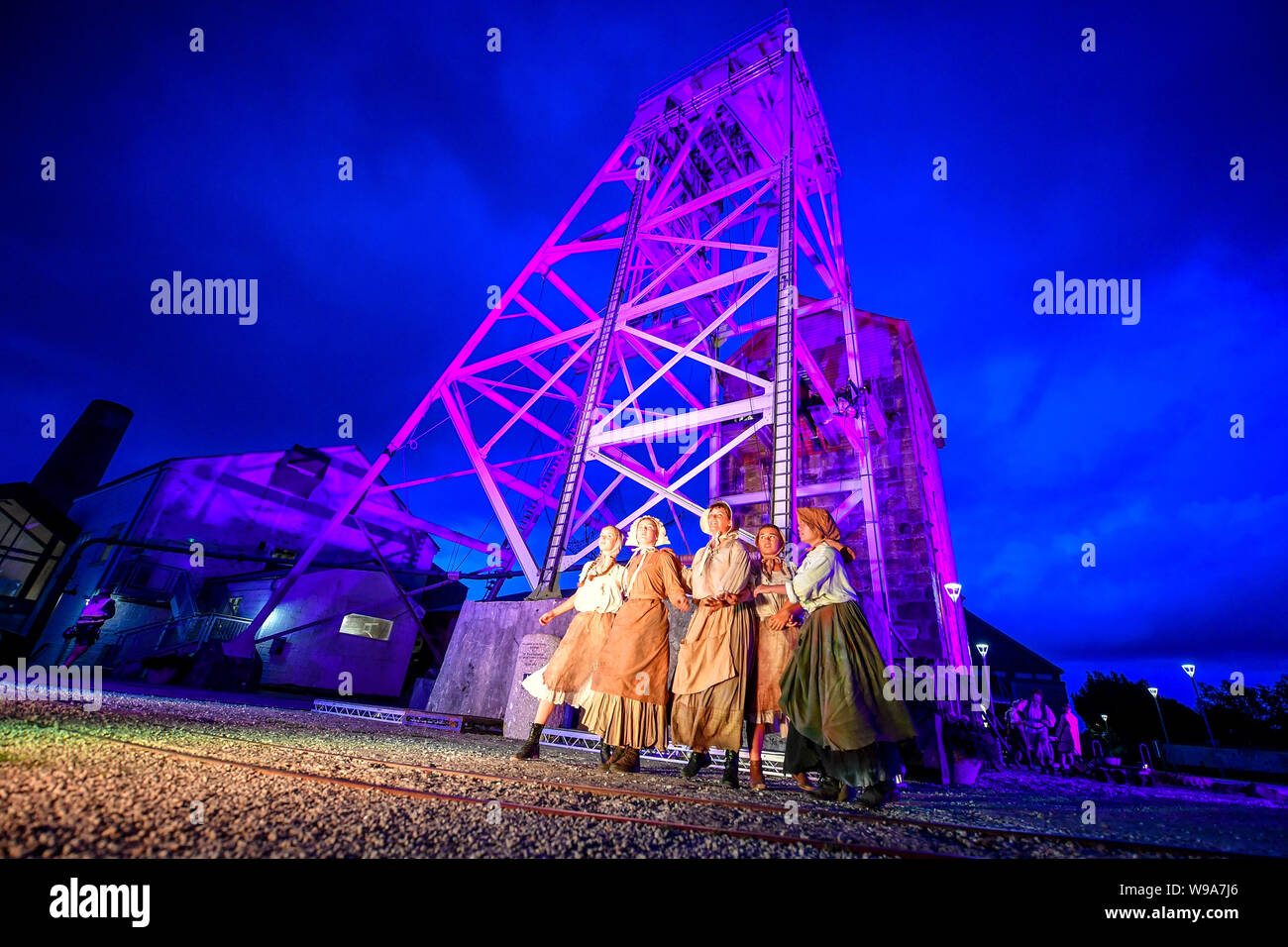 Performers rehearse around the base of a mining pit headframe in between acts of the theatrical performance of Estah???s Story, which is set in the old mine workings at Heartlands World Heritage Site, Cornwall, featuring aerial performances, song and spoken word, retelling stories from the Cornish mining industry in the 1800s. Stock Photo