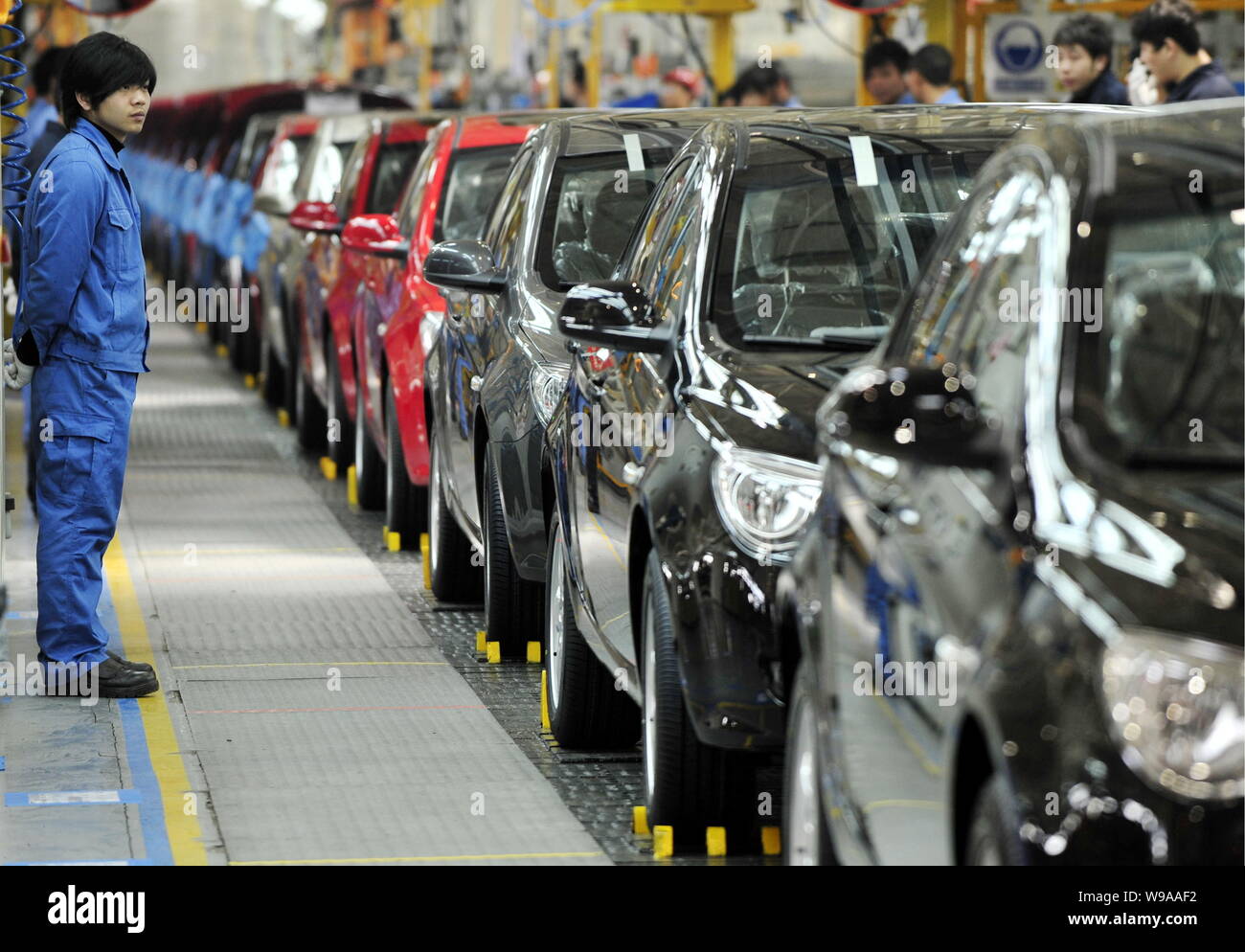 Chinese factory workers look at Roewe 350 cars going through the