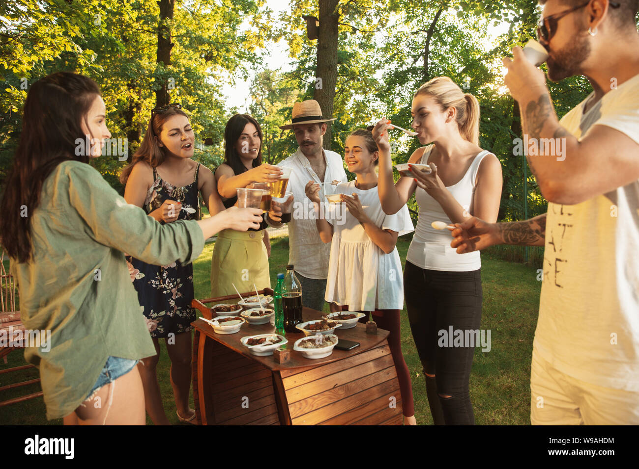 Group of happy friends eating and drinking beers at barbecue dinner on