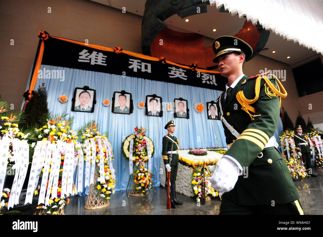 A Chinese paramilitary policeman walks past two others standing guard in front of portraits of the eight police officers who died in the Haiti earthqu Stock Photo