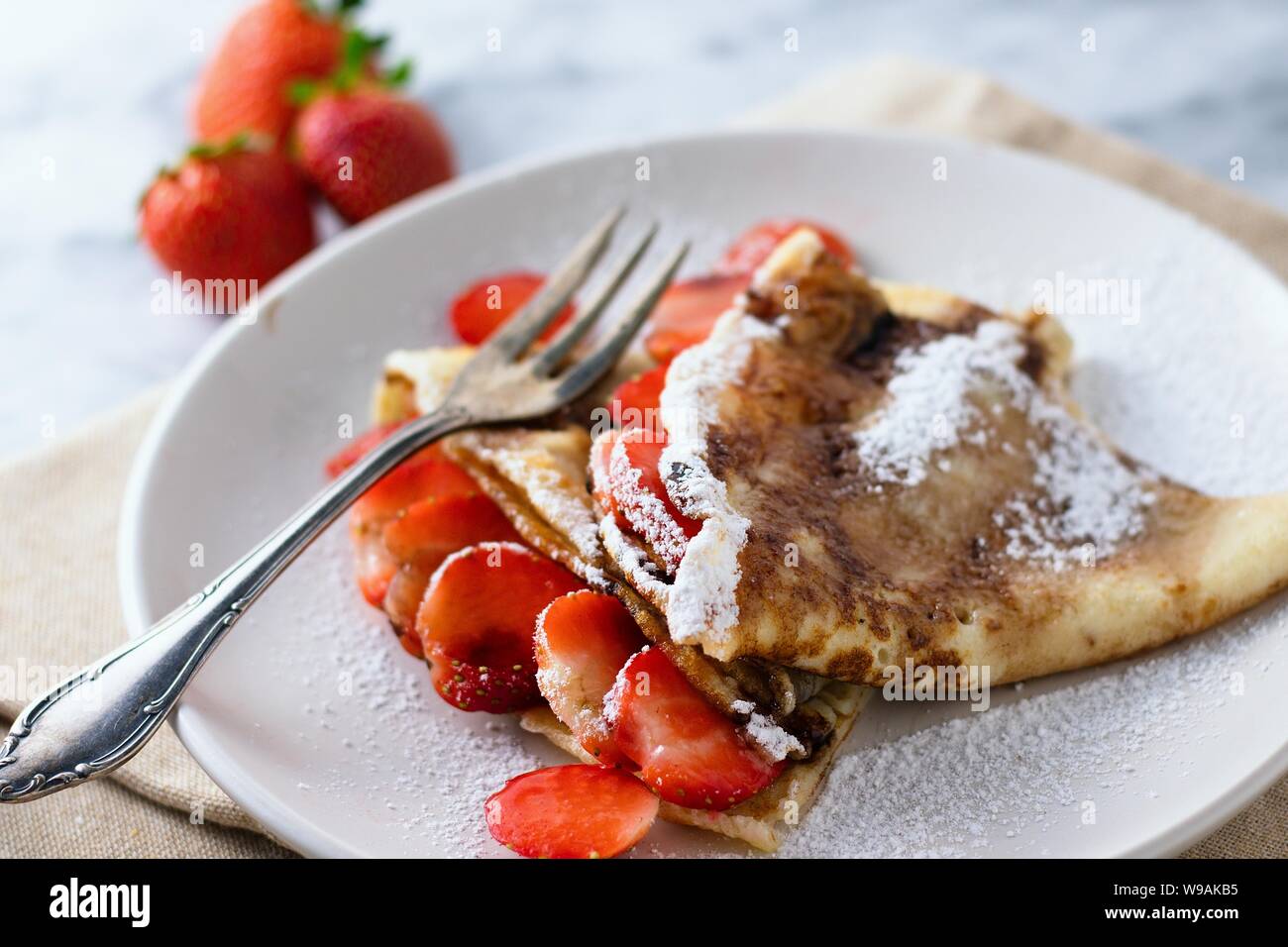 Crepes folded into triangles with strawberries and sugar coating on white plate on marble surface Stock Photo