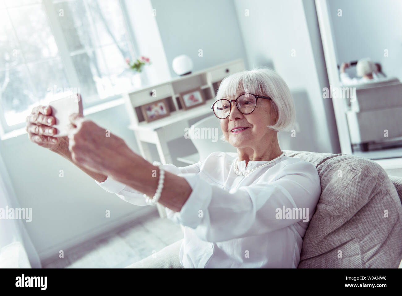 Modern beaming elderly lady holding her smartphone making selfie Stock Photo