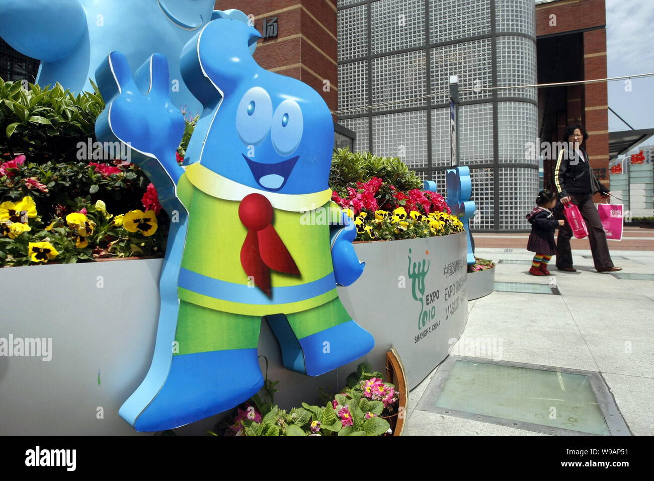 Local Chinese residents walk past Haibao figures, the official mascot of the World Expo 2010, in Shanghai, China, 17 April 2010.   The promotion song Stock Photo