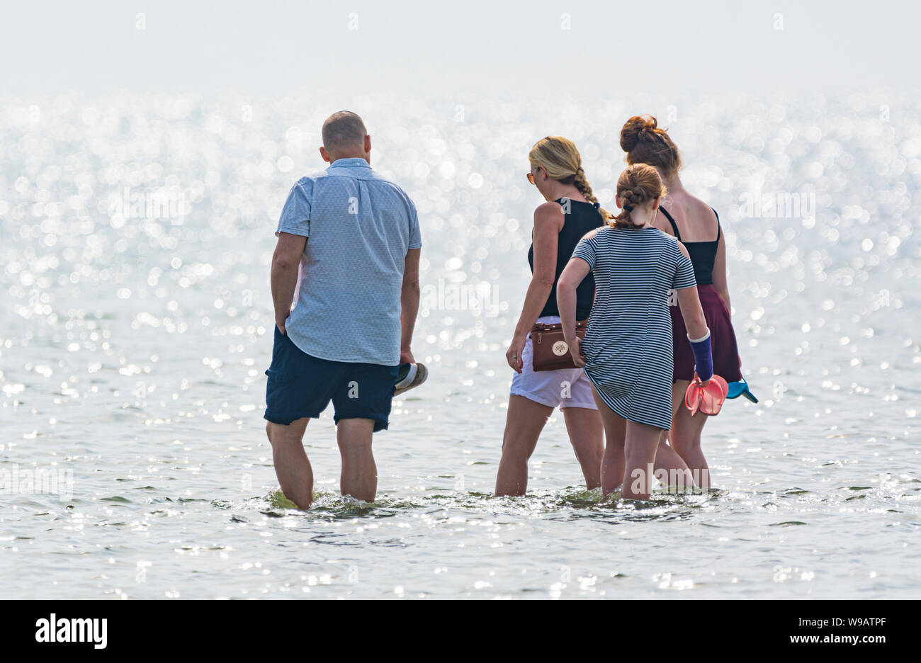 Small family of people paddling in the sea on a hot Summer day in the UK. Stock Photo