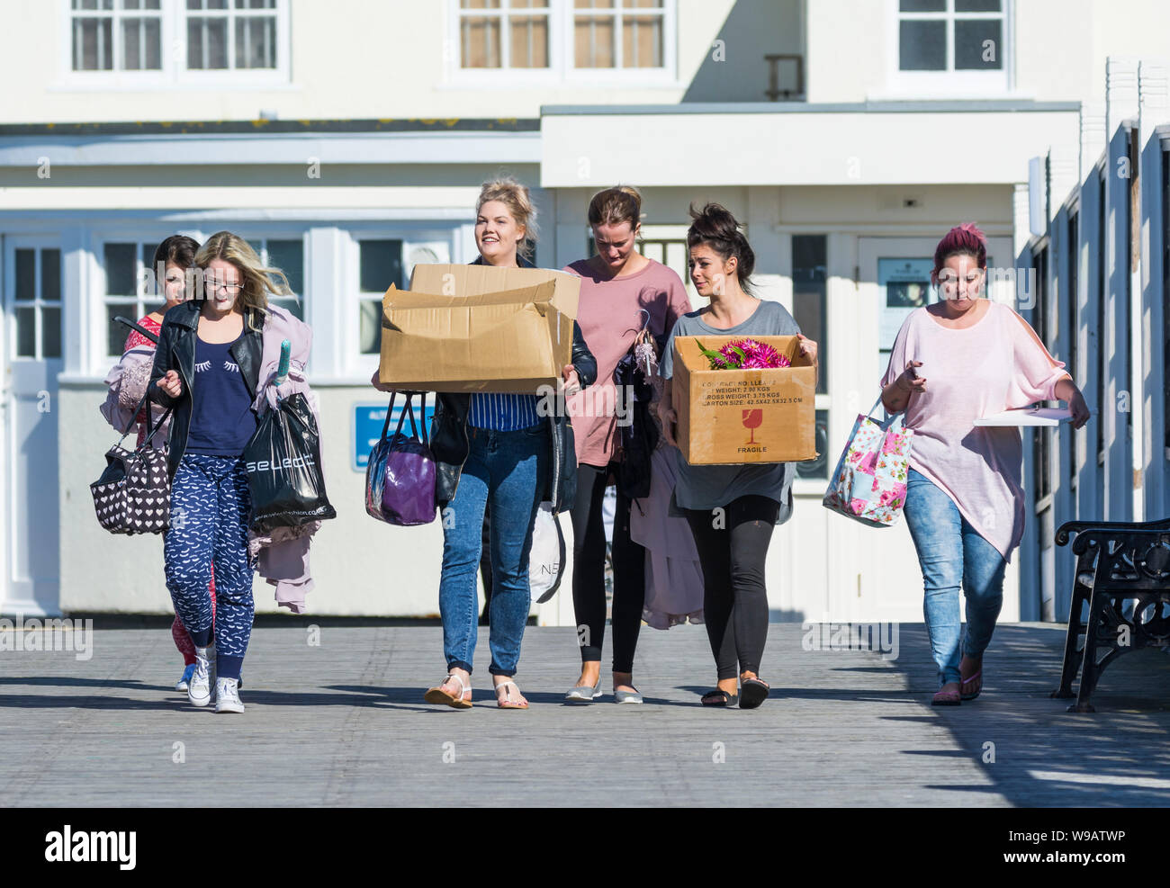Group of young women or teenagers walking while carrying boxes, probably going to an event or party. Stock Photo