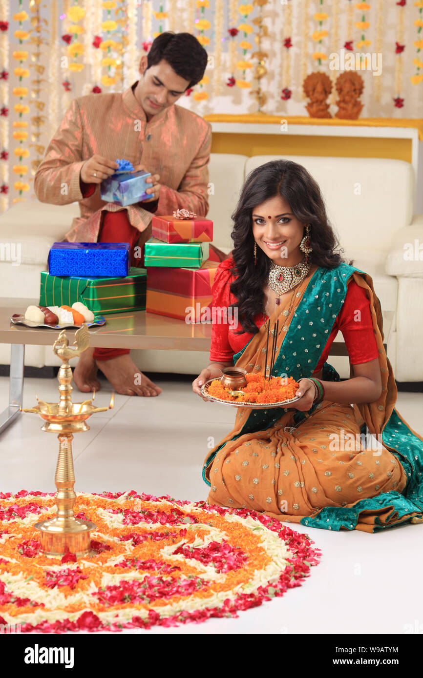 Young woman making rangoli with her husband packing gifts in the background Stock Photo