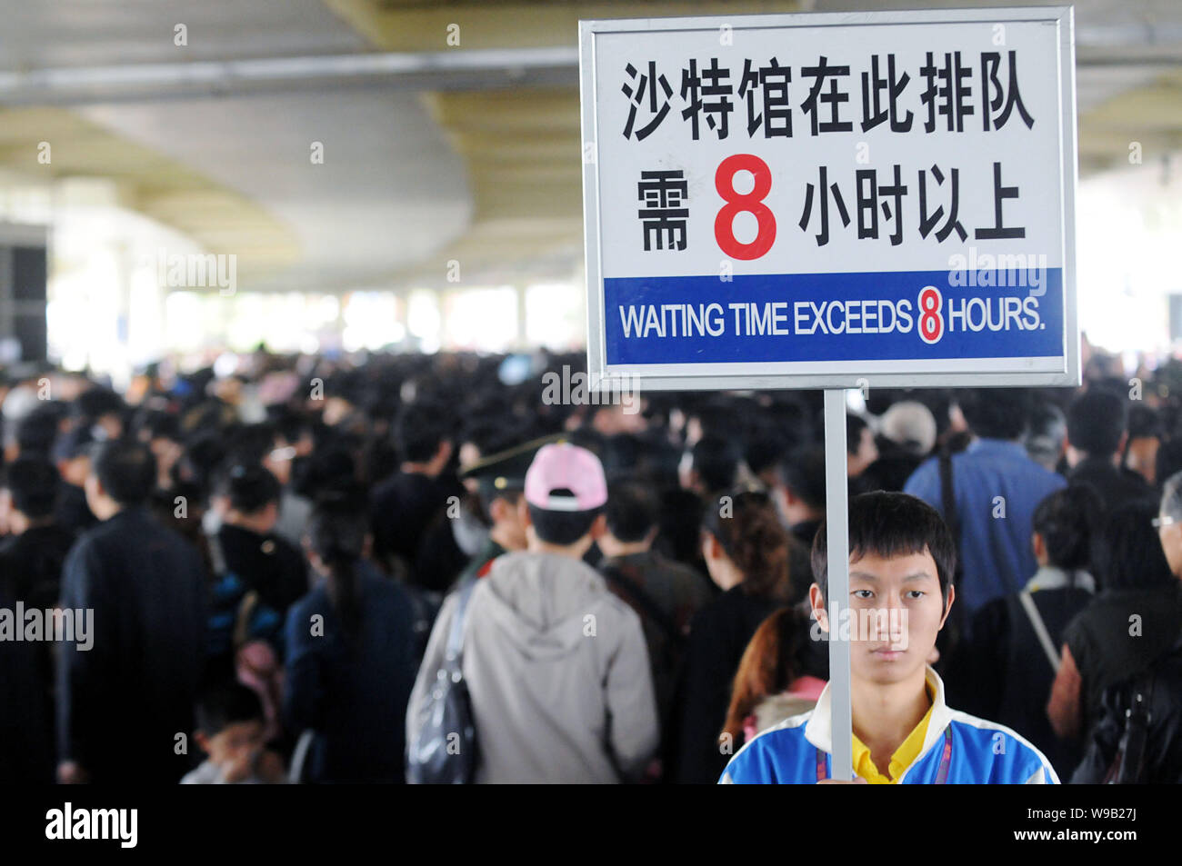 A Chinese staff holds up a placard reading Waiting Time Exceeds 8 Hours next to crowds of visitors queuing up to enter the Saudi Arabia Pavilion in th Stock Photo