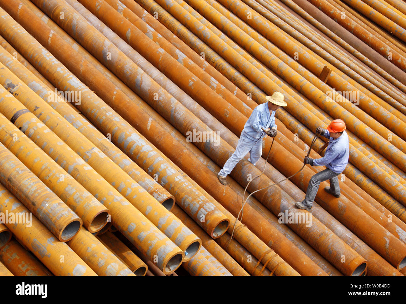 --FILE--Chinese workers stand on a stack of steel pipes at a steel ...