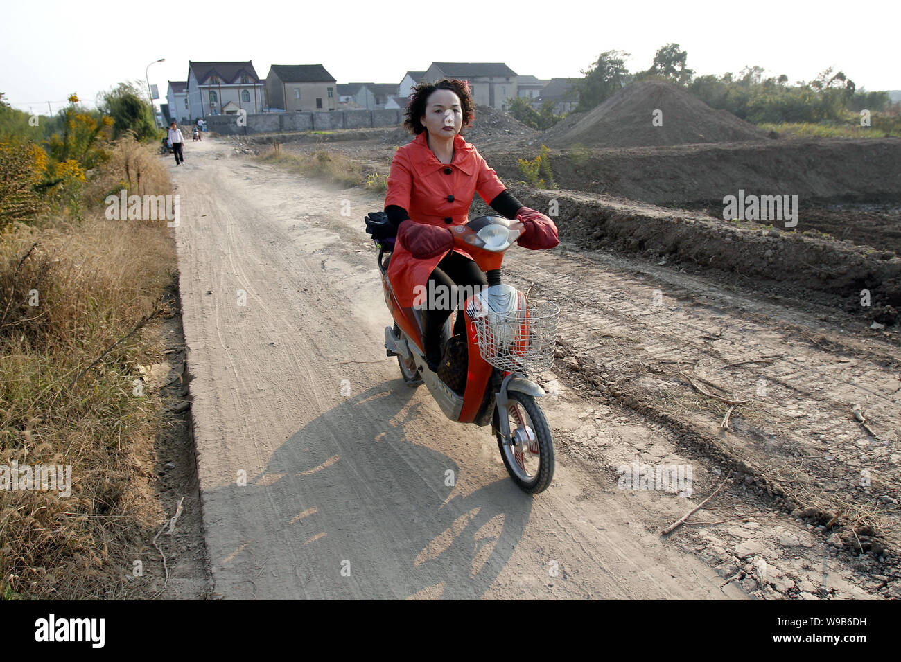 A Chinese woman rides her electric bike past the site on which a Disneyland theme park will be built in Chuansha town, Pudong, Shanghai, China, 5 Nove Stock Photo