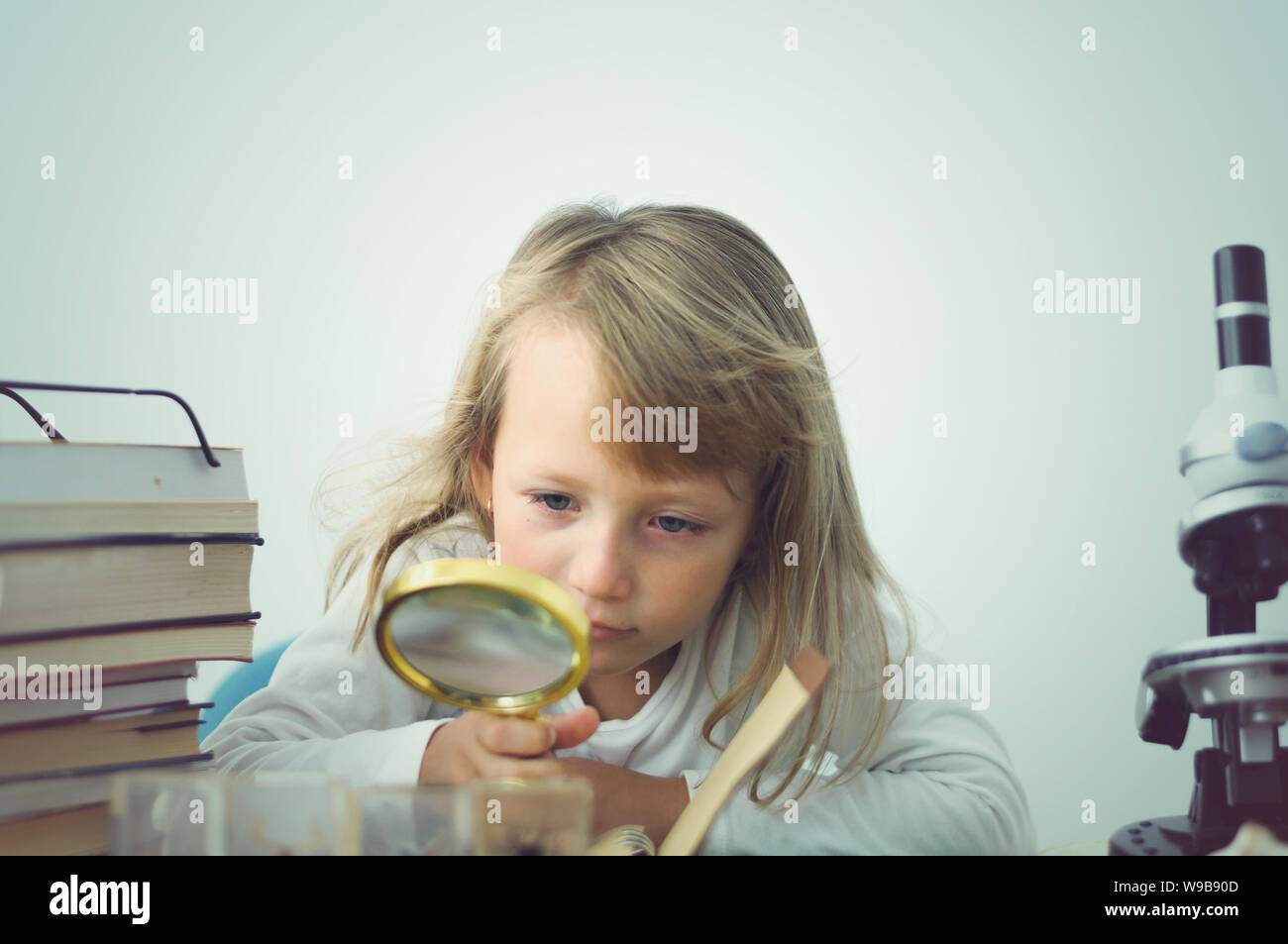 little girl playing scientist among stacks of books with a microscope