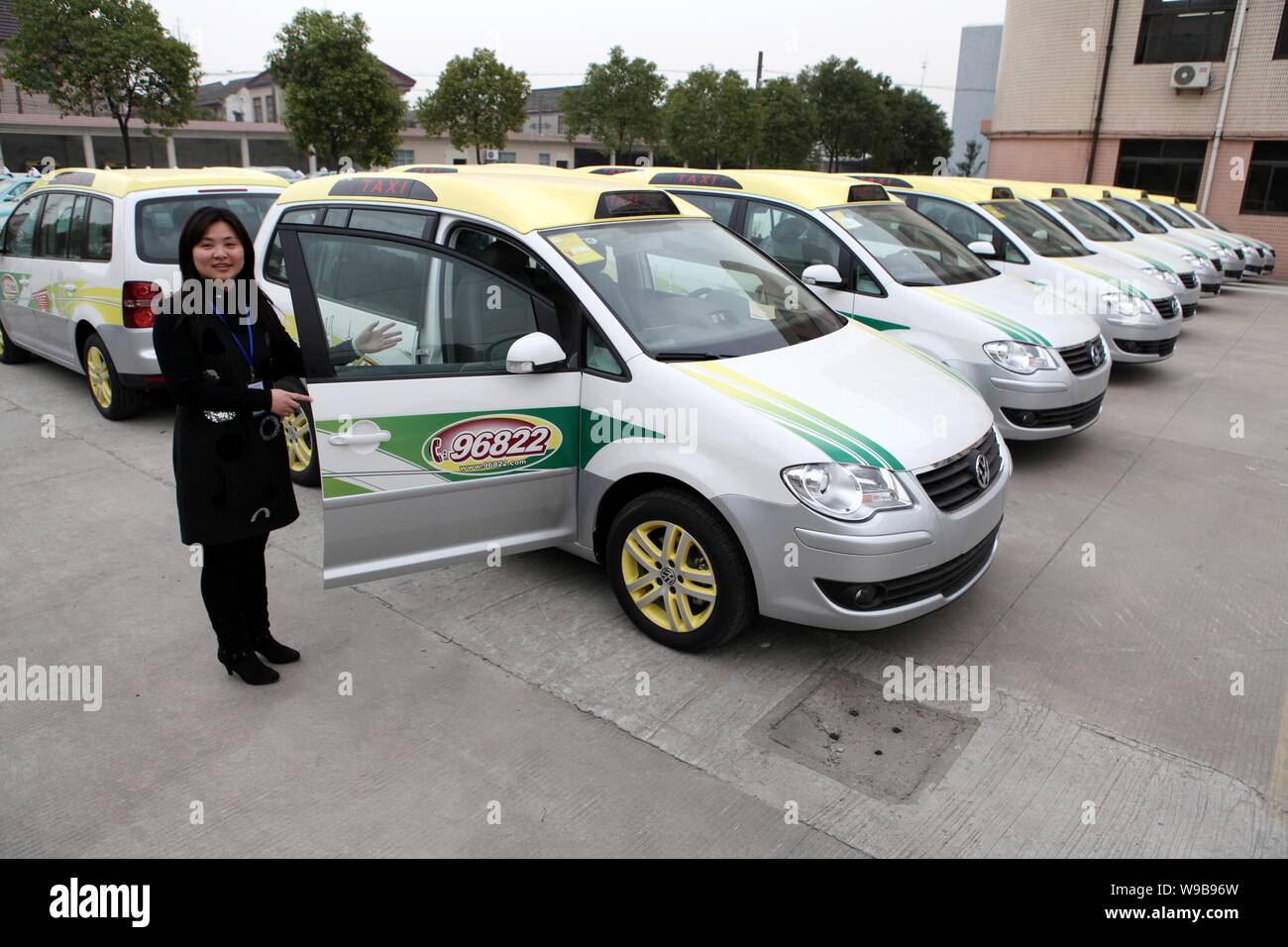 A Chinese woman stands next to Volkswagen Touran taxis for the Expo 2010 lined up at a parking lot in Shanghai, China, 22 March 2010.   Shanghai has f Stock Photo