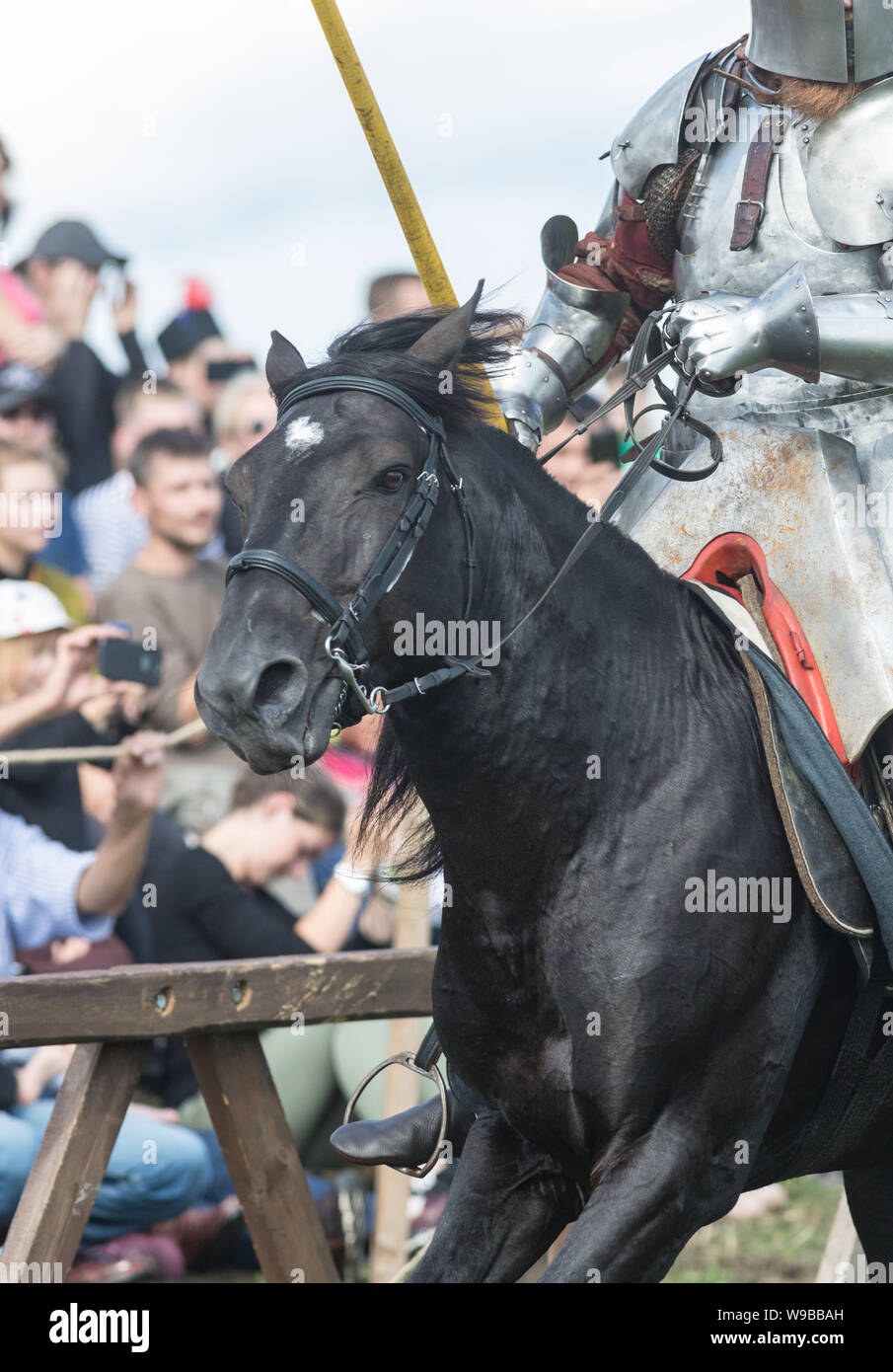 A man knight involved in a fight riding a horse - people watching behind the fence Stock Photo