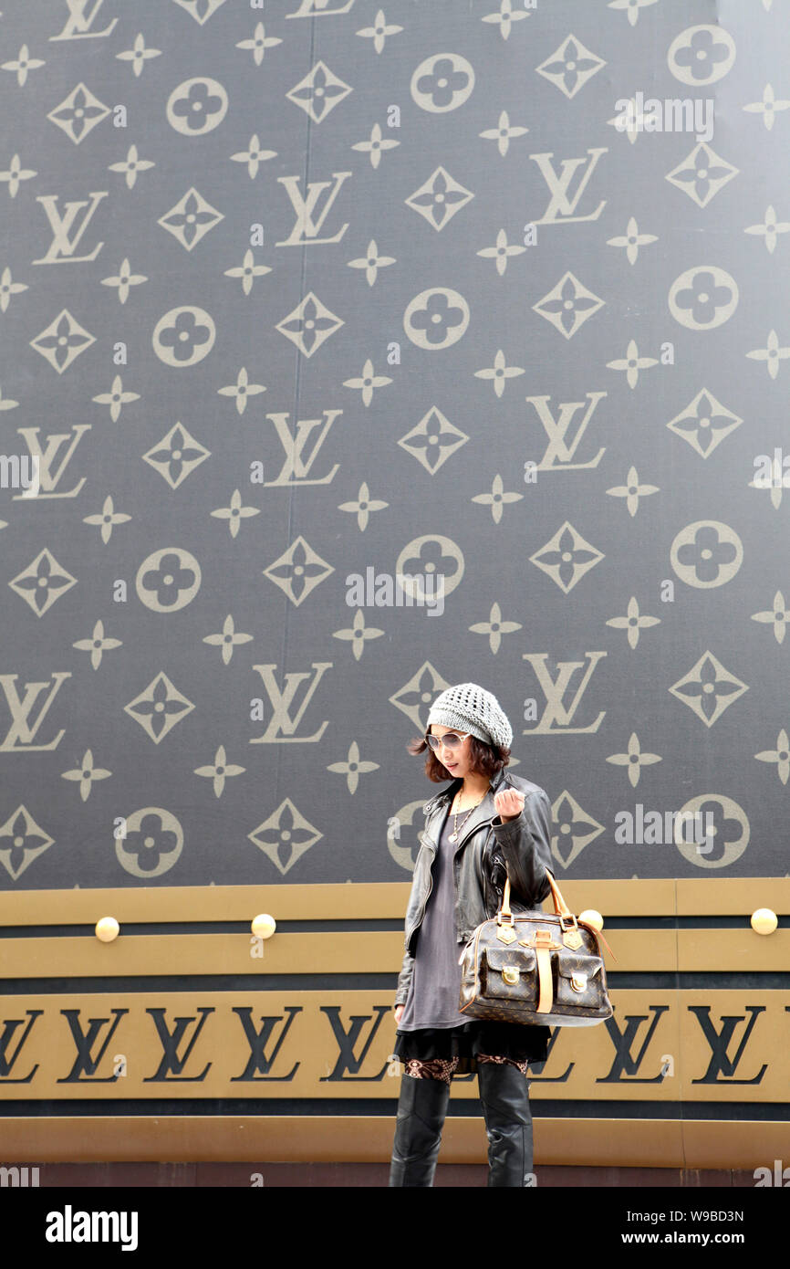 A trendy young woman carrying a Louis Vuitton (LV) handbag walks