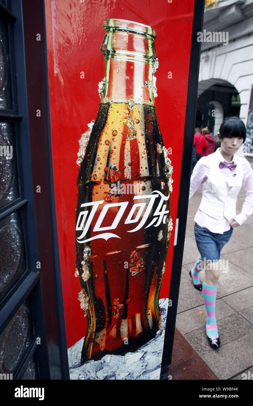 A young Chinese woman walks past an advertisement for Coca-Cola coke in ...