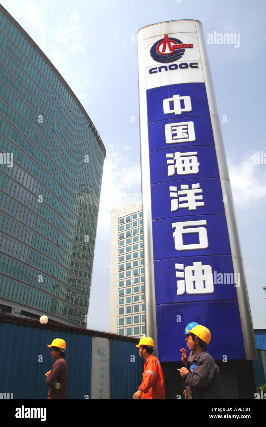 Chinese workers walk past a name board of China National Offshore Oil ...