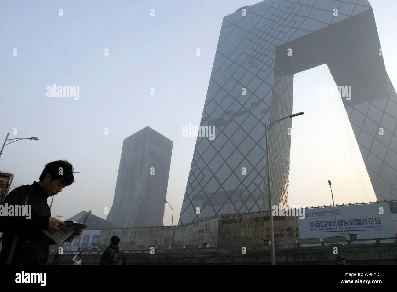 Local Chinese citizens walk past the new CCTV Tower and the damaged Mandarin Oriental Hotel building after the fire in Beijing, China, Tuesday, 10 Feb Stock Photo