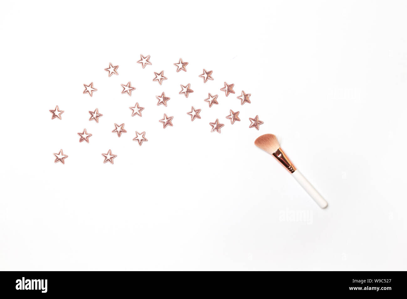 Make up brush on a pastel pink background with gold glitter stars. Flat lay top view copy space. Stock Photo