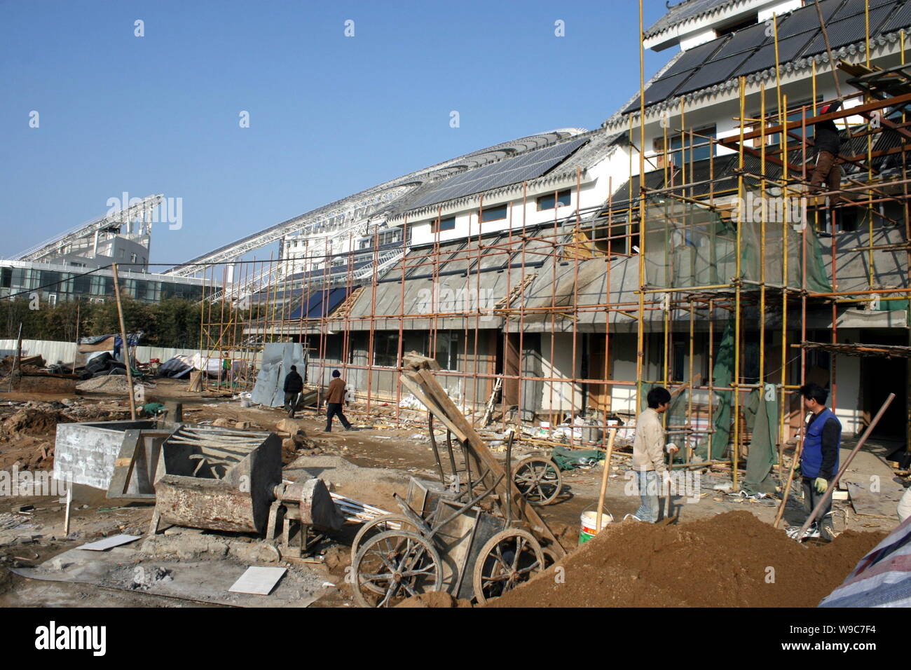 Chinese construction workers are seen scaffolding to install solar heat pipe collectors and solar panels on the rooftop of a building in the Solar Val Stock Photo